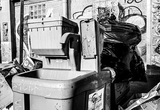 Portable sink in Skid Row missing soap dispenser surrounded by trash