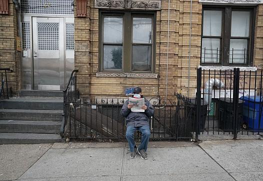 man reading newspaper outside apartments