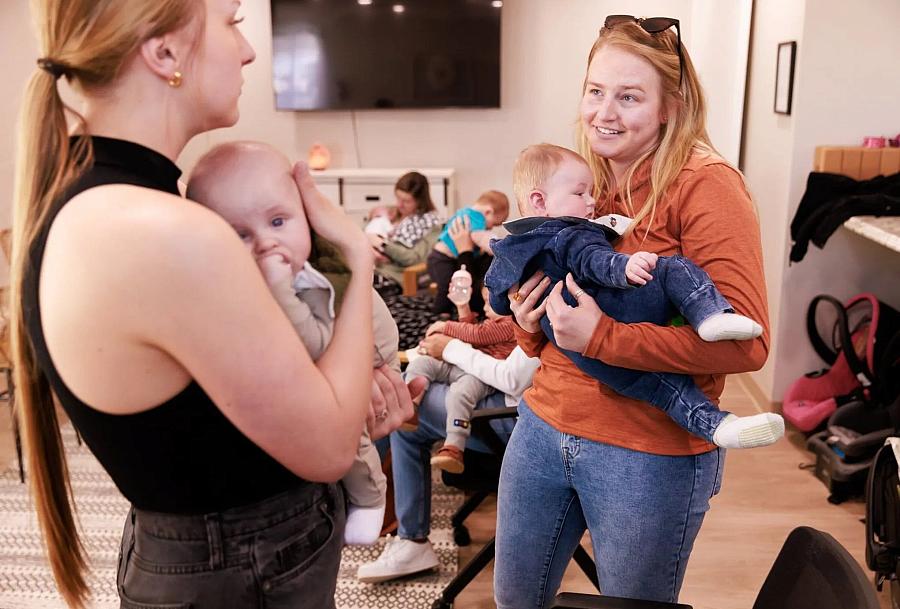 Two women holding their babies, talking to each other