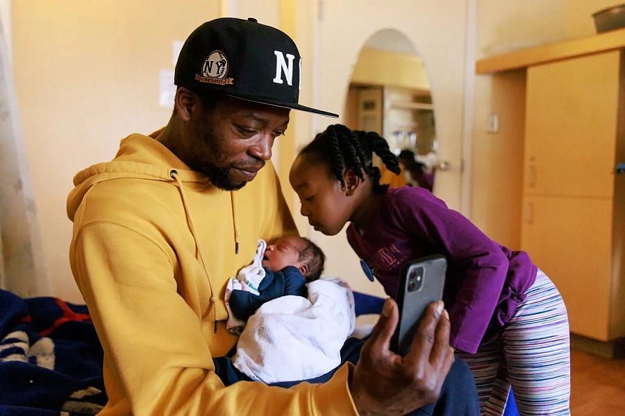 A father holding one-day old son and 5 year old daughter looking at his son