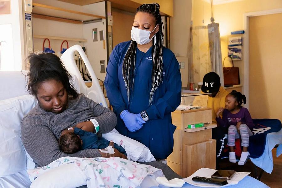 Mother breastfeeding her baby and health care worker is standing helping her.