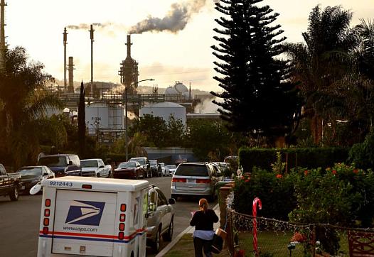 A mail carrier works in the shadow of the Phillips 66 refinery in Wilmington, California.