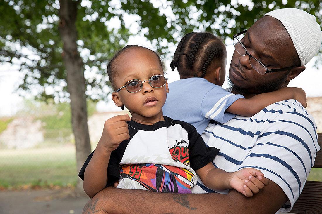 (Left to Right) Jihad and Murad sit with their dad, Andrew Irby, in the park. Irby worries about the future of his twin sons.