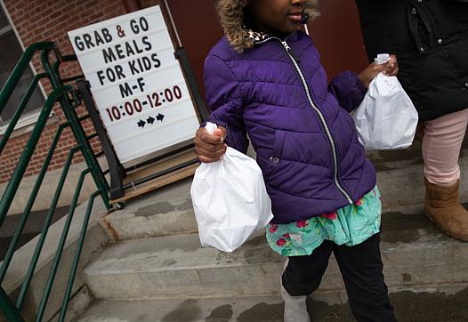 A student carries home bagged meals given out as part of a grab-and-go meal program run by public schools in Stamford, Connectic