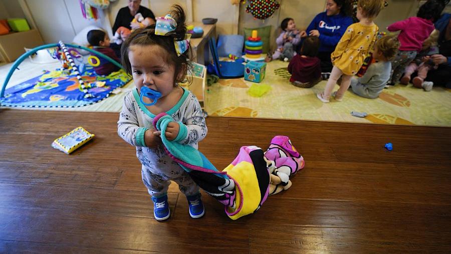 Girl child with towel in her hand and other kids playing behind in preschool