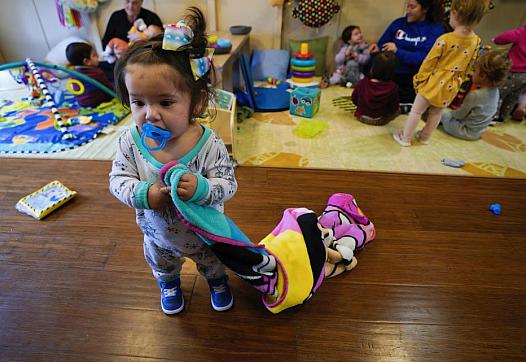 Girl child with towel in her hand and other kids playing behind in preschool