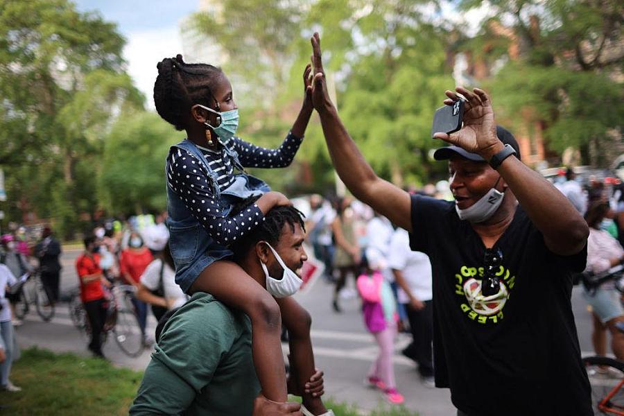 Child sitting on a man's shoulder giving a high-five to another person.