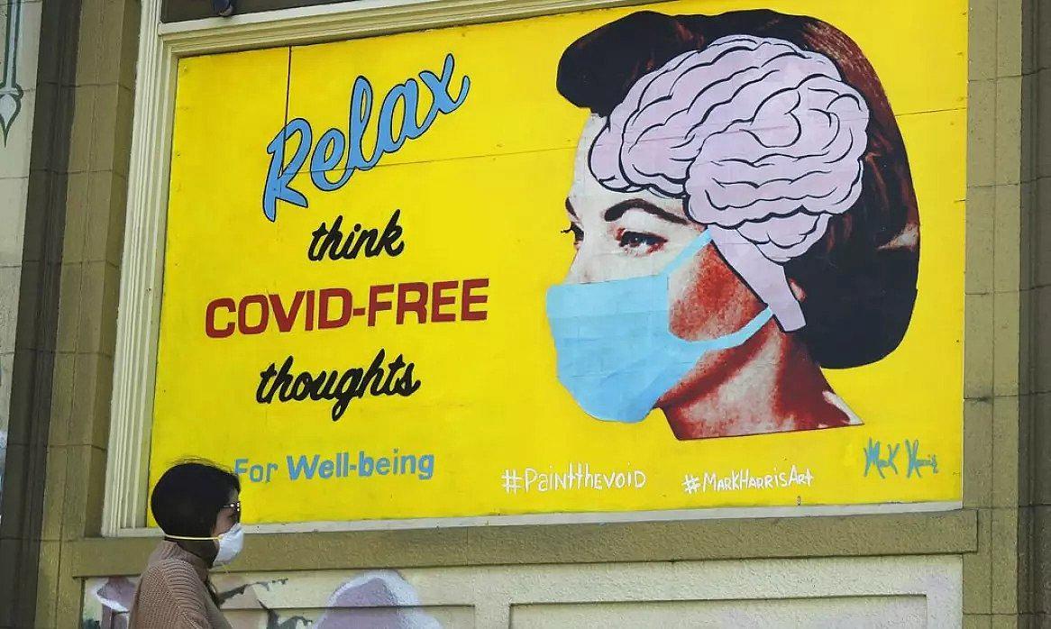 A woman wears a face mask while walking under a sign that reads "Relax think COVID free thoughts" during the coronavirus outbrea