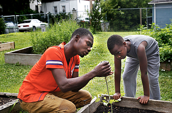 Nate Collins, 19, left, helps Deonta Williams, 9, prepare to plant a tomato plant on a Saturday in July at "We Got This," a prog