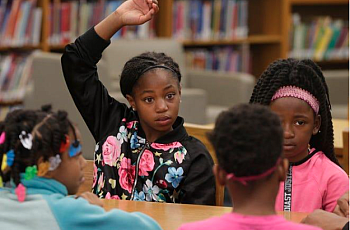 A child, sitting with other children, raising hand