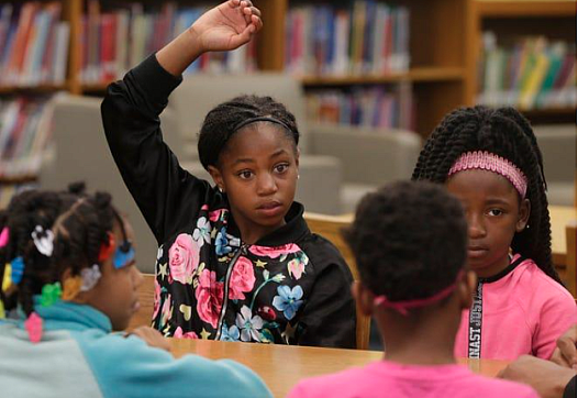 A child, sitting with other children, raising hand